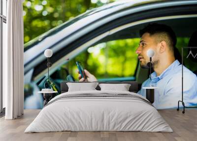 Young Man driving and looking message in his smart phone. Wall mural